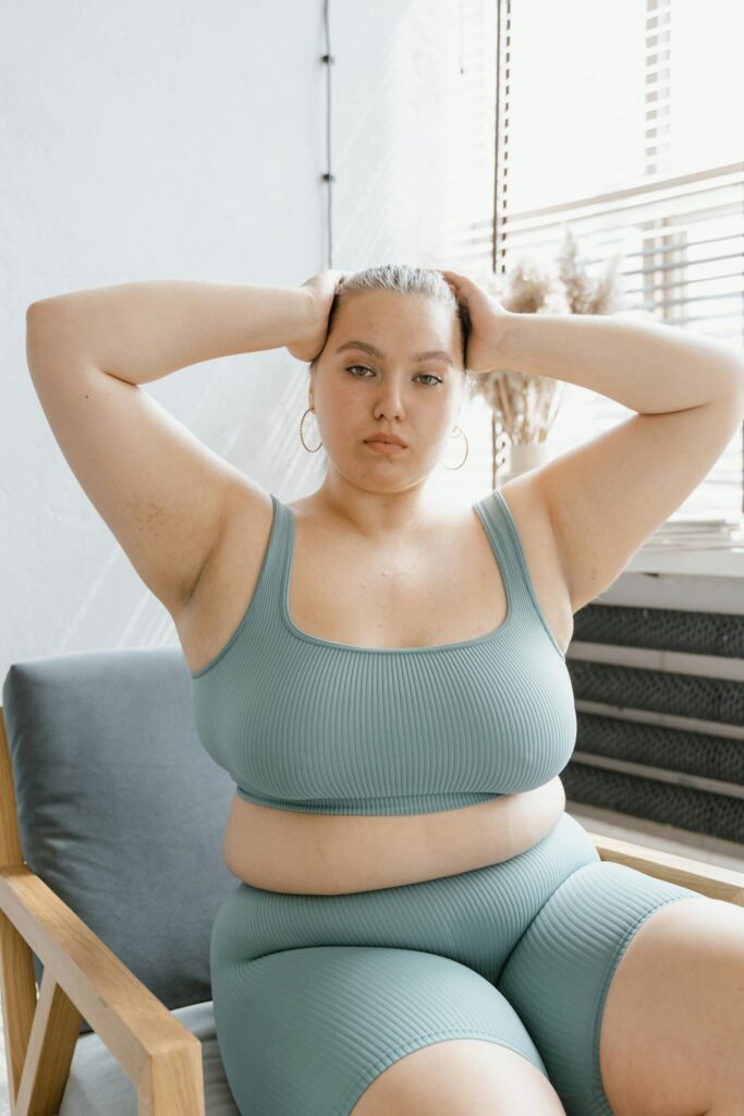 A confident plus size woman in a sports bra poses indoors, promoting body positivity.