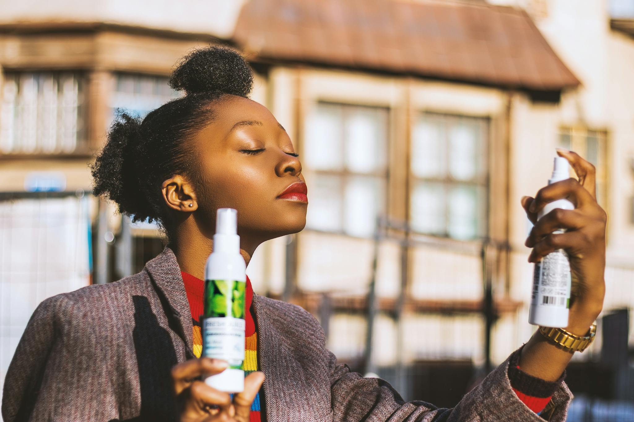 A stylish woman using refreshing spray bottles outdoors, exuding elegance and relaxation.