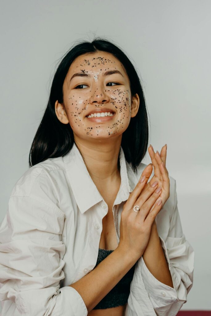 Asian woman smiling with a glittery facial mask during a studio photoshoot.