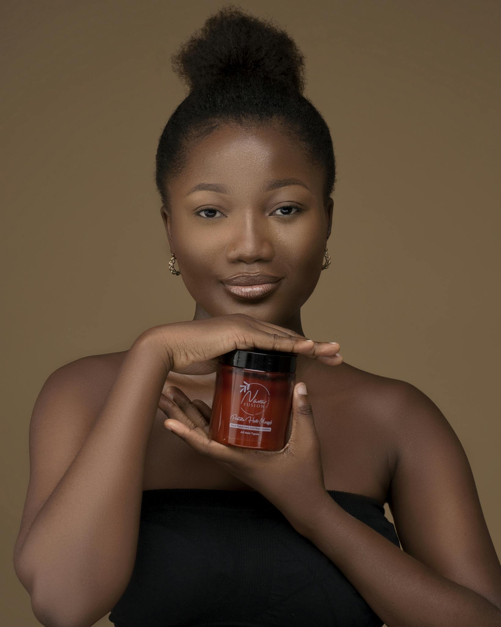Elegant studio portrait of a woman holding a cosmetic jar with a neutral background.