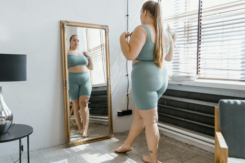 Plus size woman in activewear admiring her reflection in a mirror indoors.