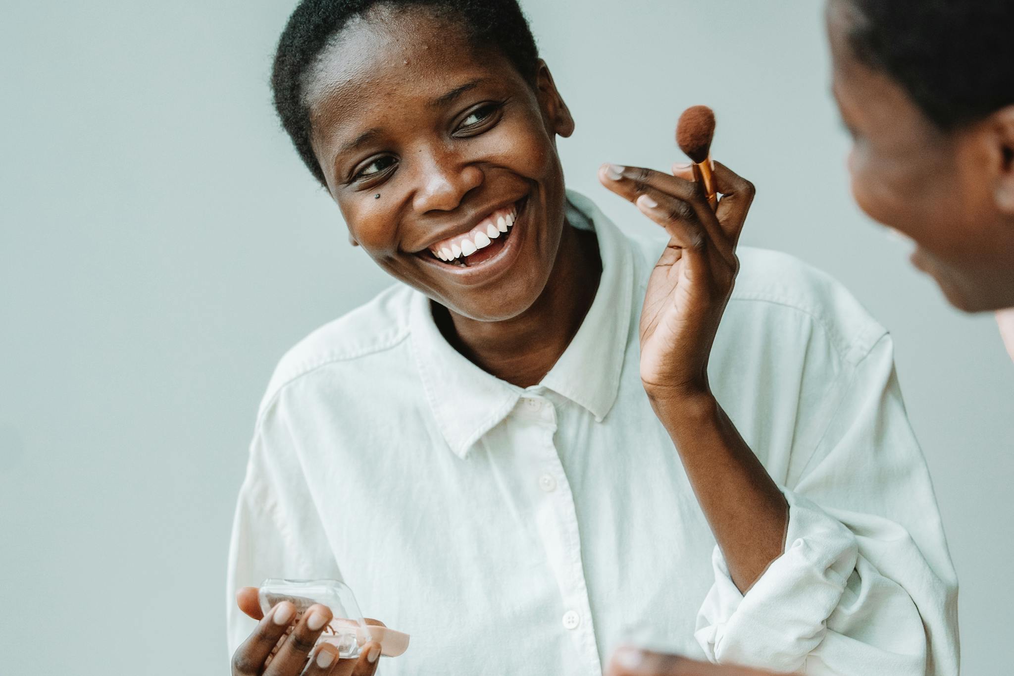 Smiling woman applying makeup with a brush, showcasing beauty and happiness.